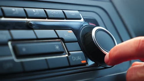 Hand adjusting temperature of air conditioner in car.