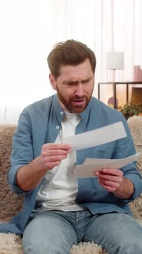 Distressed Man Reads Bad News on Couch at Home