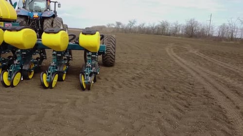 Blue tractor with yellow seeder working on the field in Ukraine OA