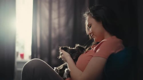 Woman Holding and Petting Small Dog Indoors
