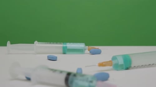 Pills Falling Near Syringes on White Surface