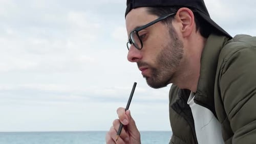 Young Man Ponders with Pencil by the Sea