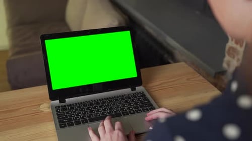 Female Specialist Working on a Laptop with a Green Screen Mockup Display in a Home Living Room