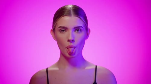Joven traviesa saca la lengua, mira a la cámara, toma de estudio, violeta