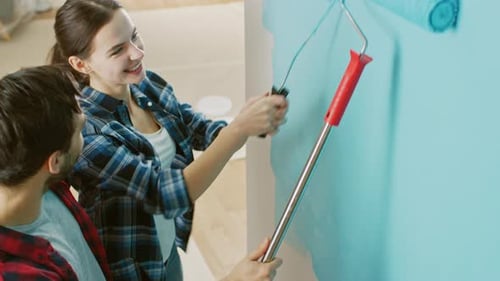 Young Beautiful Couple Decorate Their New Apartment. Husband and Wife are Painting the Wall with Ro