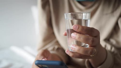 Woman Holding Water Glass and Phone Indoors
