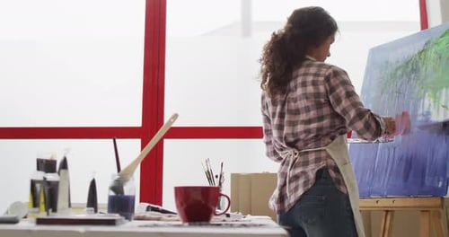 Video of biracial female artist painting in studio