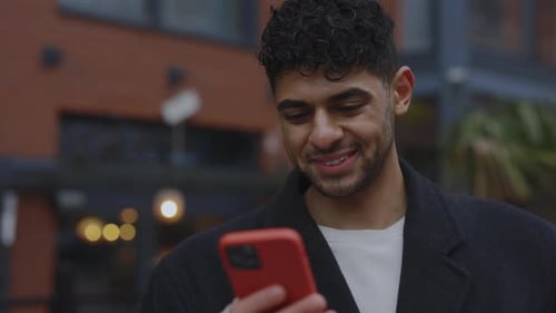 Smiled Multi Ethnic Man Standing Outside and Using Smartphone Texting