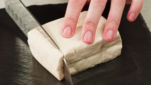 Slicing fresh firm Tofu on black cutting board