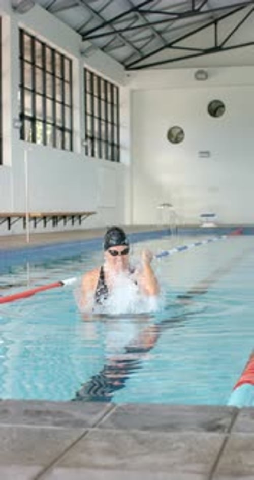 Vertical video: Swimming in indoor pool, woman celebrating victory with raised fist