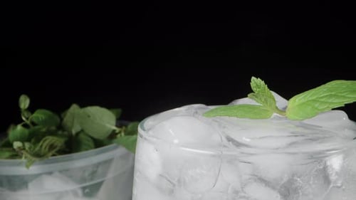 A container of mint and a glass of soda on the table. mint leaves on ice. Dolly slider extreme close