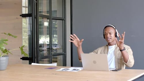 Using laptop and wearing headphones, man having video conference in modern office