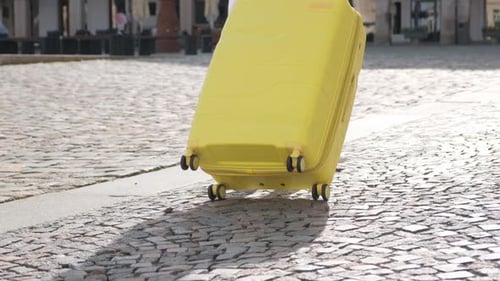 Rear View of Elegant Woman Walking in Old City Pulling Yellow Suitcase