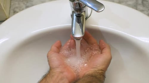 Open tap in the sink with water falling into hands. Top view washbasin.