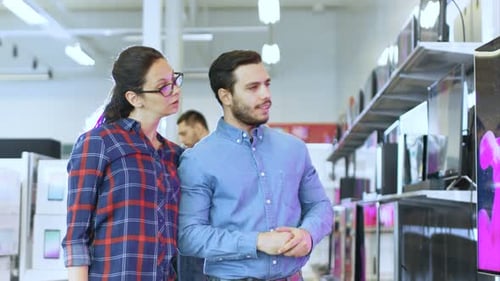 Young Couple Shopping for a New 4K Television Set in the Electronics Store. They're Deciding on the