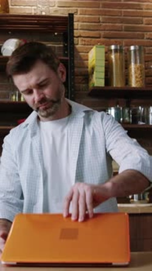 Man Opens Laptop in Bright Kitchen Setting