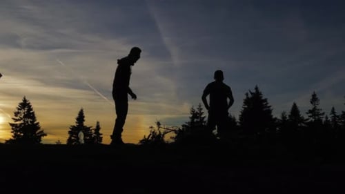 Panning right-to-left on an epic sunset view in the mountains with two hikers and some pine trees in