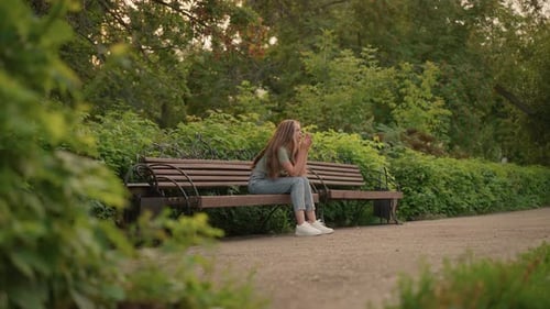 Reflective Woman Sitting on Park Bench Surrounded By Greenery in Peaceful Setting