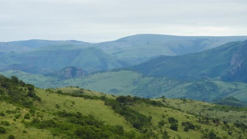 Weite afrikanische Landschaft mit üppigen grünen Hügeln, fernen blauen Bergen und Tälern auf einem wolkigen Sommer
