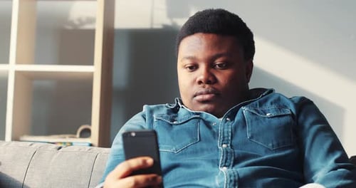 Young Man Relaxing on Couch Using Smartphone