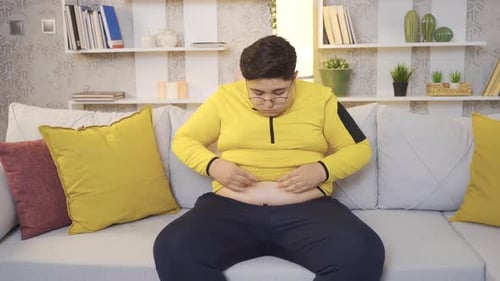 Young Adult Sitting on Couch Touching Stomach