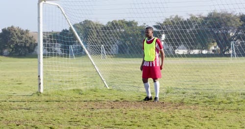 Portero en uniforme de fútbol de pie frente al poste de la portería en el campo