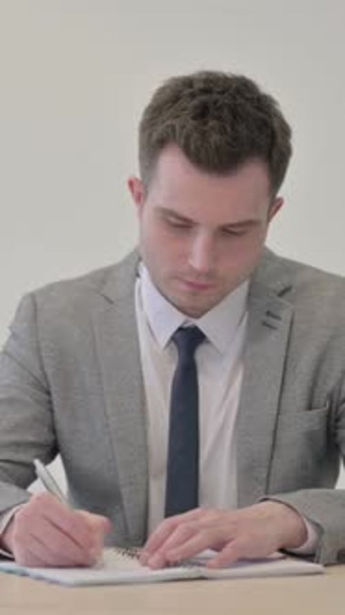 Young Man in Suit Writing in Notebook at Desk