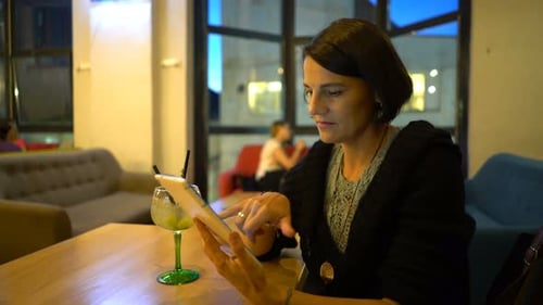 Young woman browsing on tablet computer in modern cafe one evening
