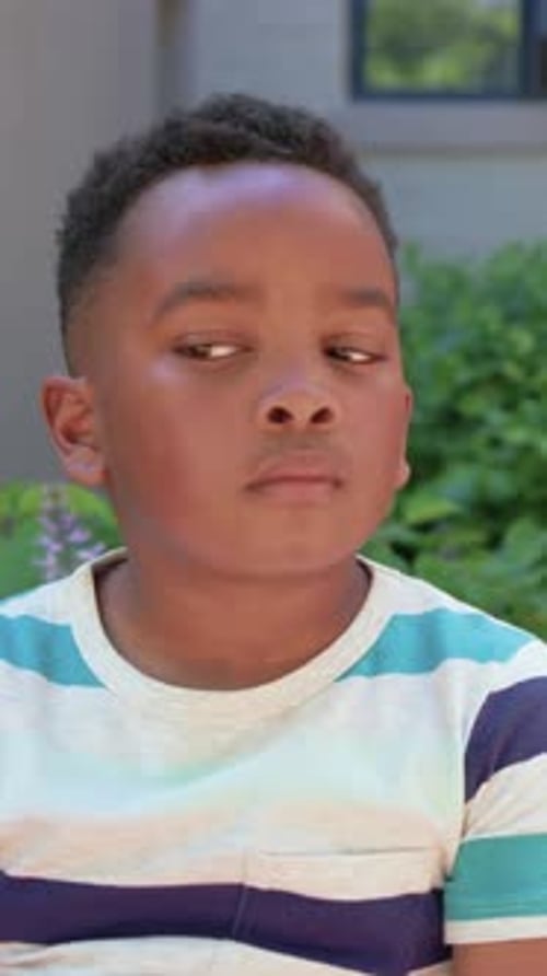 Vertical video: Hearing offscreen voice sitting boy glancing listening smiling on patio striped tee