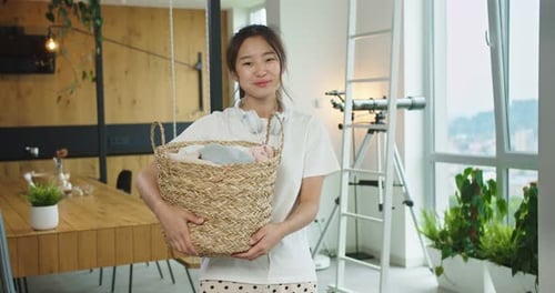 Close Up of Happy Cheerful Young Beautiful Asian Woman with Headphones on Shoulders Holding Basket