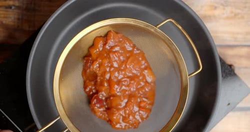 Straining Red Vegetables with Wooden Spoon in Kitchen