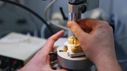 Male hands operating the machine tool producing plaster denture. Close up. Dentistry concept.
