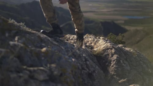 Male hiker climbing up rocky mountain, closeup of walking boots footsteps