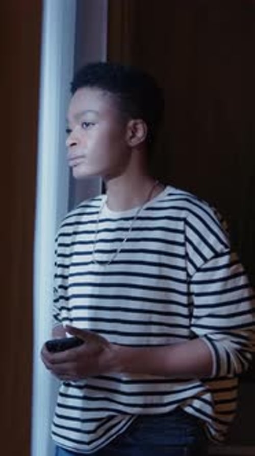 Beautiful Young African American Woman Stand Near Window Using Smartphone or Cell Phone in Modern