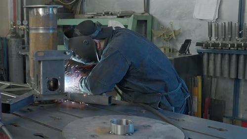 Welder in workshop repairs structure with sparks