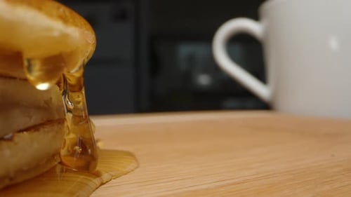 A stack of pancakes drizzled with honey and a mug on the table. Dolly slider extreme close-up.