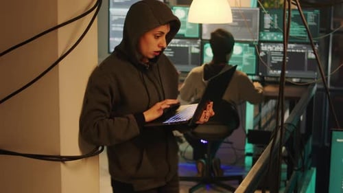 Two Hooded Figures Coding in Dark Server Room