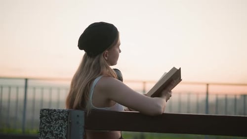 Woman Reads Book on Bench During Sunrise