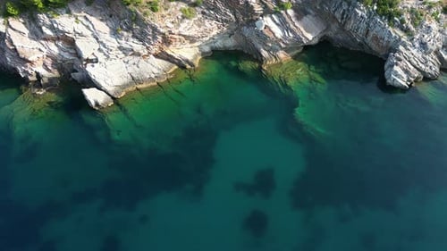 The drone flies along the sharp rocks standing by the sea. Transparent sea. Aerial view.