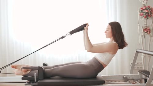 Woman Doing Pilates Exercise on Reformer Machine