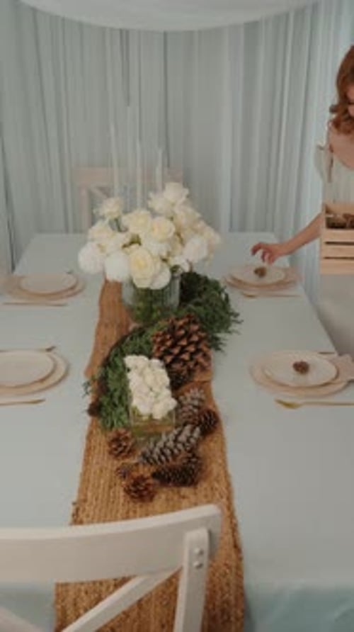 Woman Setting Elegant Table with Flowers and Pinecones