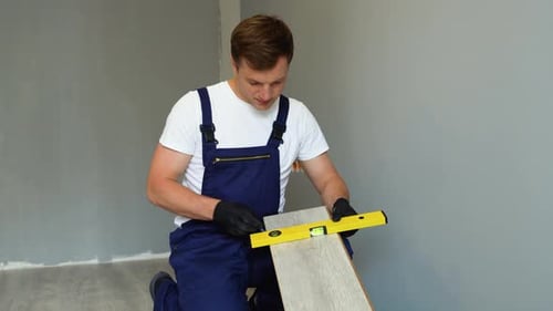 Man Installing Wood Flooring with Level and Pencil