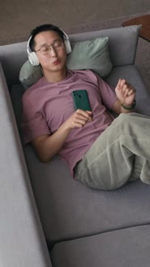 Relaxed Man Listening to Music in Headphones Resting on Couch, Top View