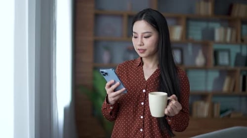 Smiling Woman Using Smartphone, Drinking Beverage at Home