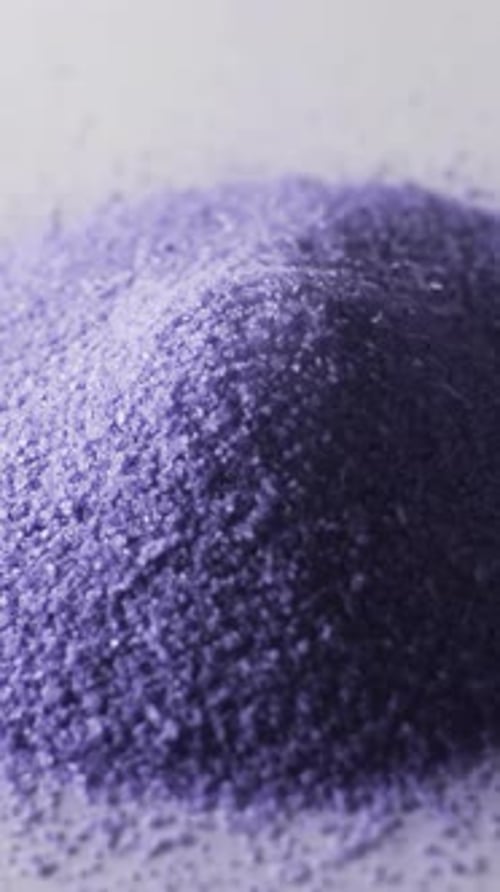 Vertical video of close up of heap of purple sand grains and copy space on white background