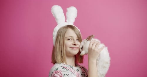 Child Cuddles with White Rabbit against Pink Background