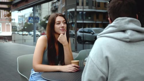 Attractive young couple having lunch sitting at cafe table outdoors, drinking coffee and talking.