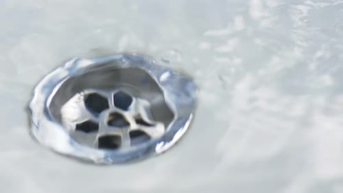 Close-up slow motion hands unplugging sink basin bowl of plug hole water draining bubbles spiral bat