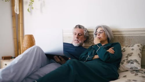 Senior Couple Relaxing and Using Laptop in Bed