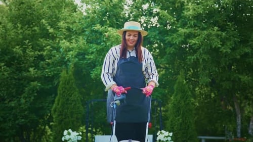 Woman Gardener Wearing Hat and Gloves Tending to Plants in a Lush Green Garden Environment
